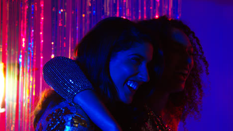 Two-Women-Friends-Having-Fun-In-Nightclub-Or-Bar-Dancing-Against-Sparkling-Tinsel-Curtain-in-Background